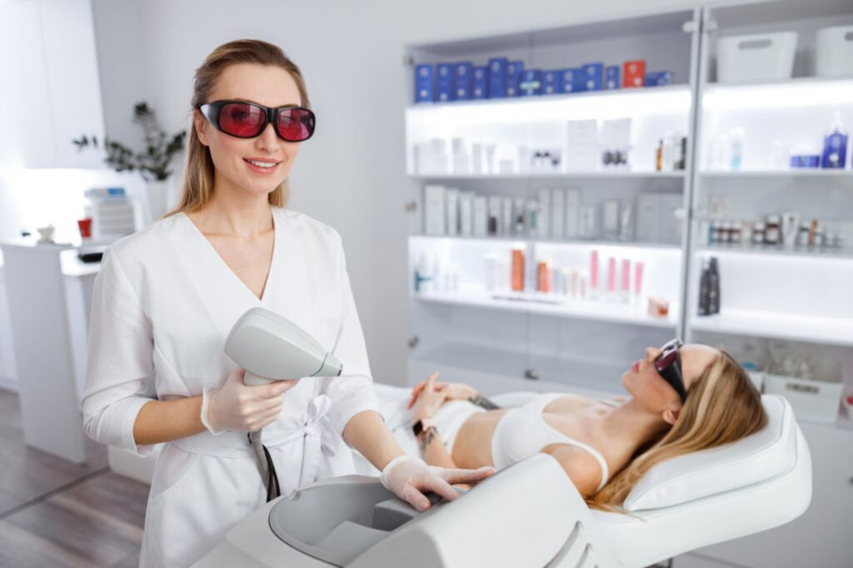 Na zdjęciu widzimy klientkę oraz kosmetologa. Kosmetolog przygotowuje się do wykonania zabiegu za pomocą lasera kosmetycznego.